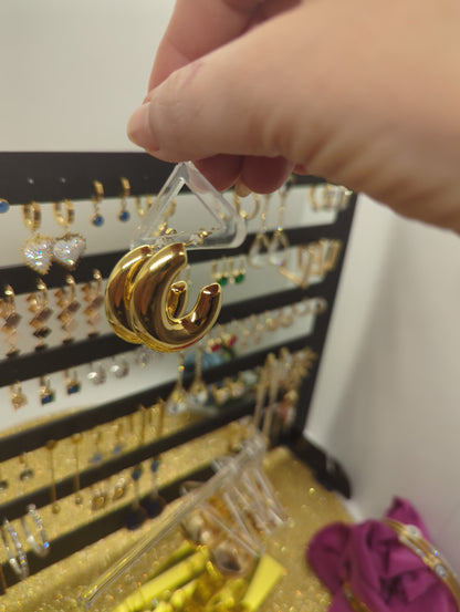 Goldene Edelstahl Creolen in der Hand vor einem Schmuckdisplay